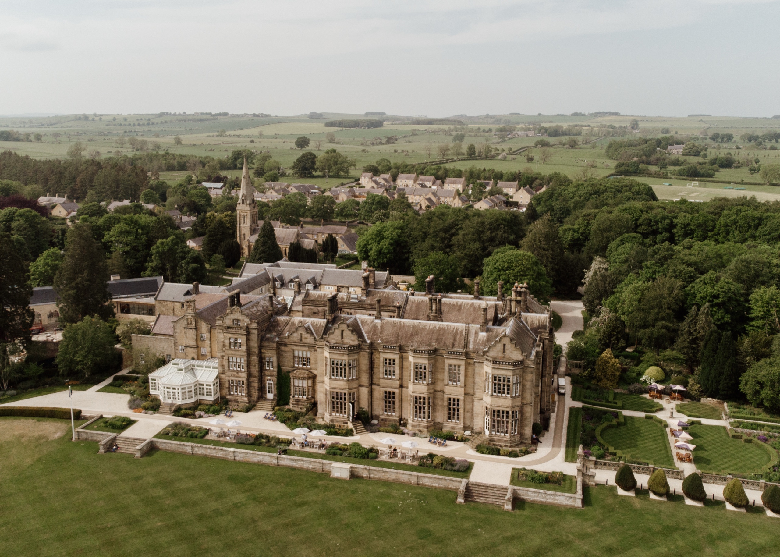 Aerial view of the hall and its formal gardens, with Matfen village and the church spire behind, Matfen Hall