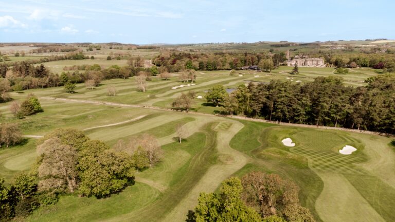 The golf course from the air, with the hall among trees in the distance and open Northumberland farmland beyond, Matfen Hall