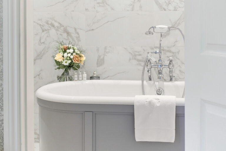 A marble bathroom with a roll-top bath and flowers, Matfen Hall