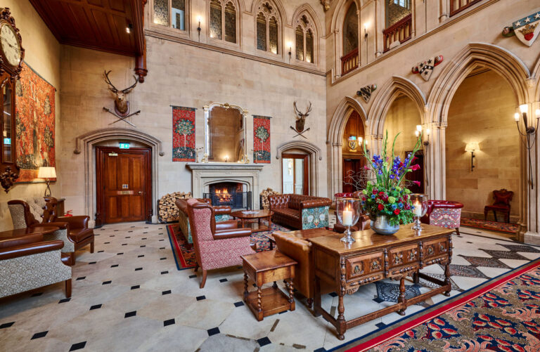 The Great Hall's stone fireplace, tapestries and antlers, with the chequered stone floor and a carved oak table, Matfen Hall