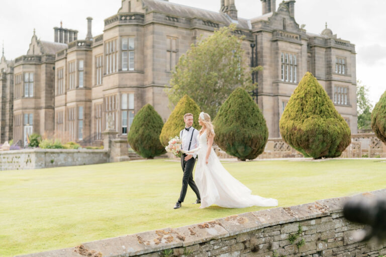 A bride and groom walking across the lawn below the hall's south front, Matfen Hall