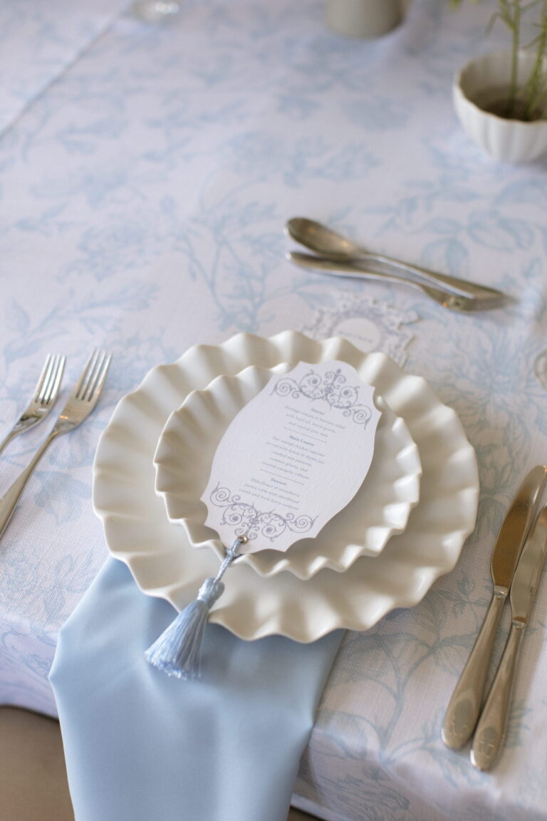 A place setting with a scalloped plate, printed menu and pale blue napkin on a floral tablecloth, Matfen Hall
