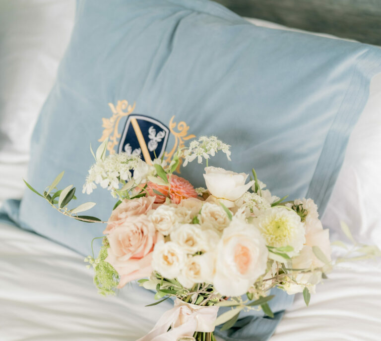 A bridal bouquet of peach roses and white flowers resting on a crested hotel pillow, Matfen Hall