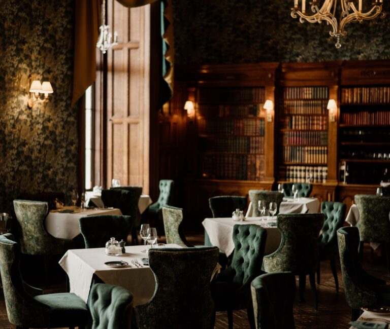 The library end of the Emerald Restaurant, with bookcases, tufted chairs and white tablecloths, Matfen Hall
