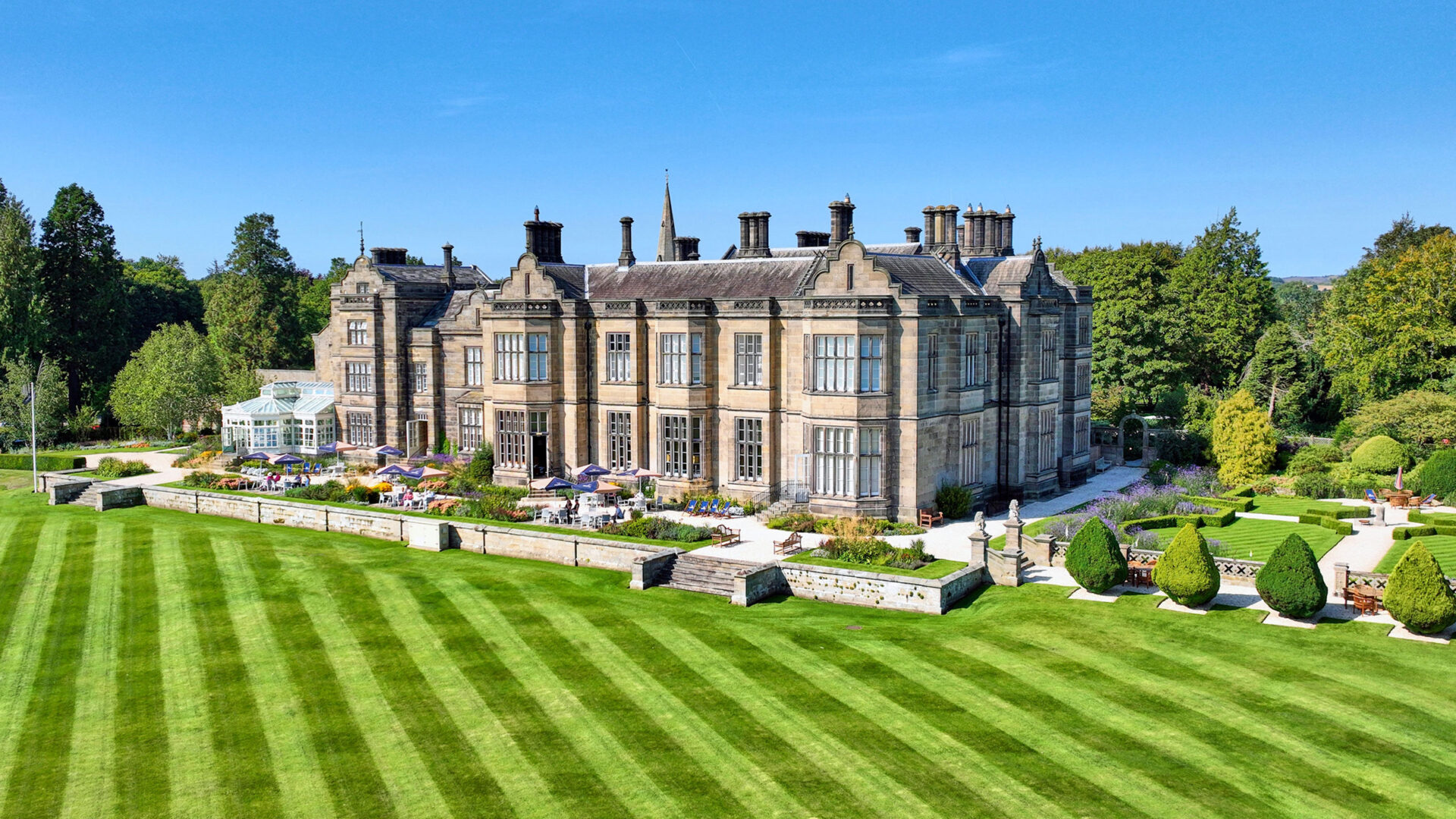 The hall seen from the striped south lawn, with the conservatory at the west end and the terraces below the house, Matfen Hall