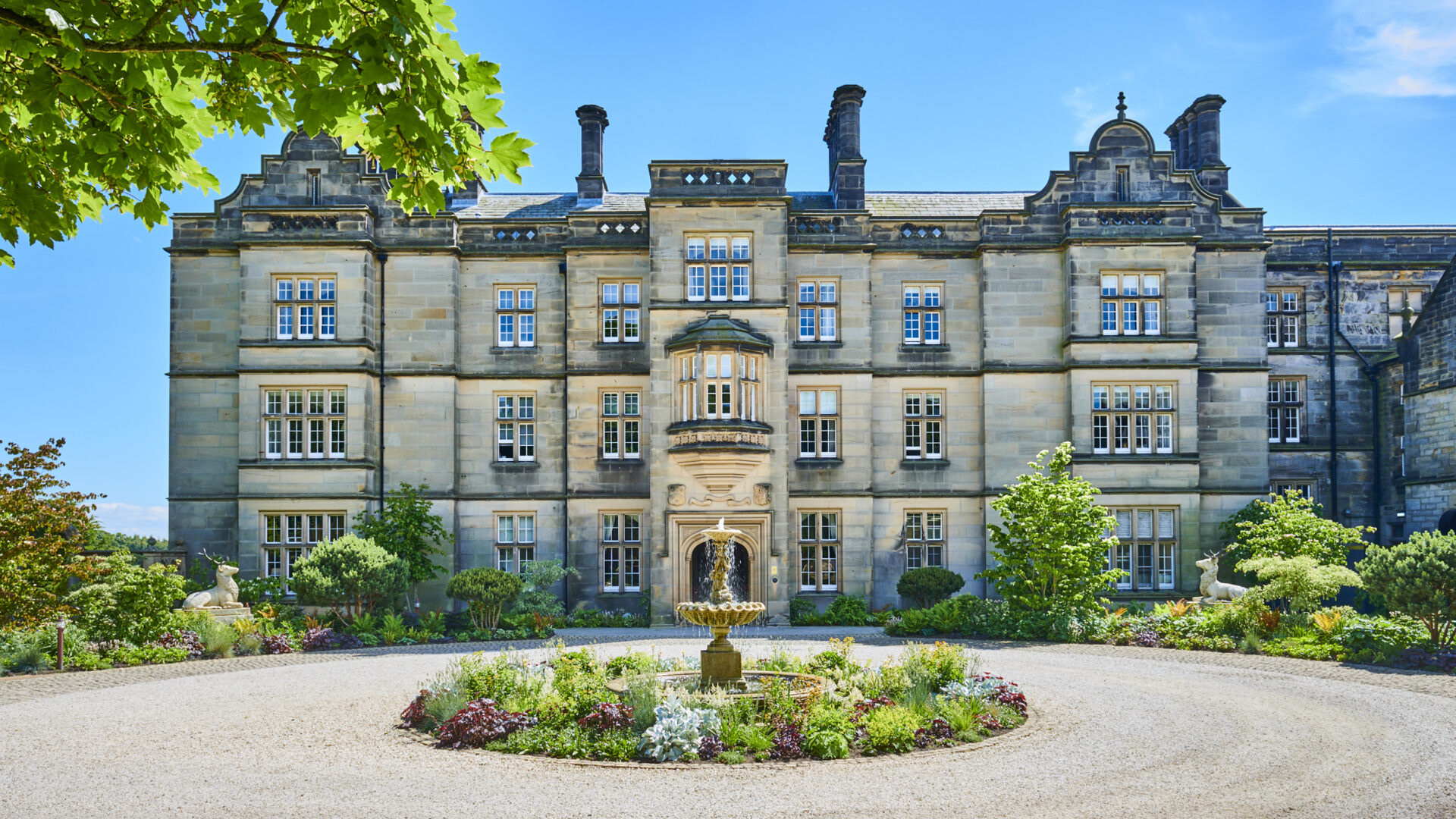 The entrance front with its central oriel window, stone fountain and circular flower bed on the gravel forecourt, Matfen Hall