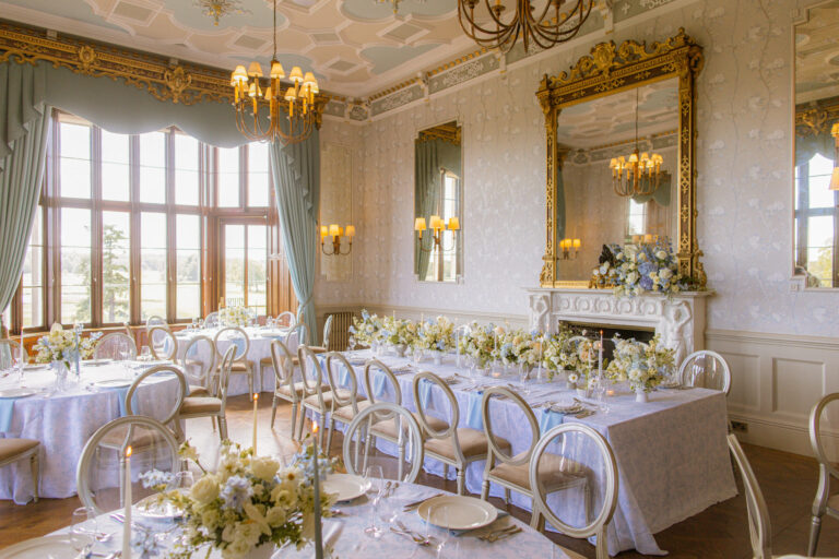 The Drawing Room laid for a wedding breakfast with long tables, white flowers and candles beneath gilt mirrors and chandeliers, Matfen Hall