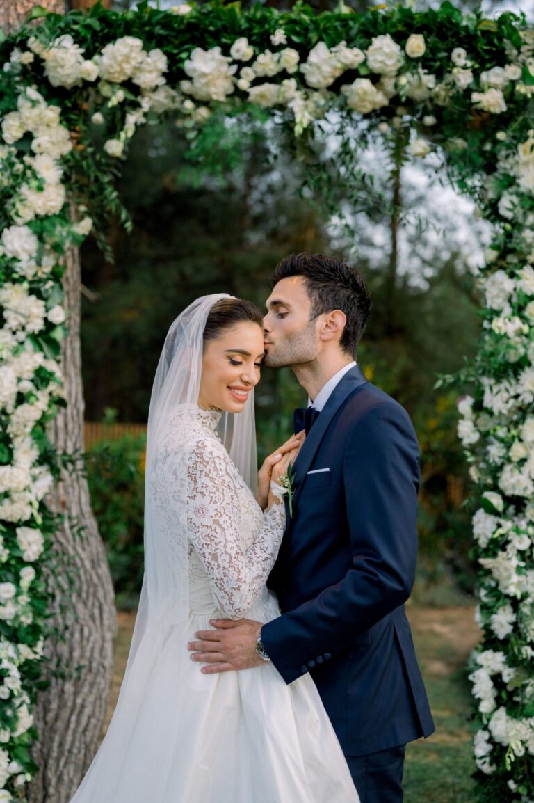 Couple beneath a floral arch of white flowers, Mathioudakis Exclusive Events