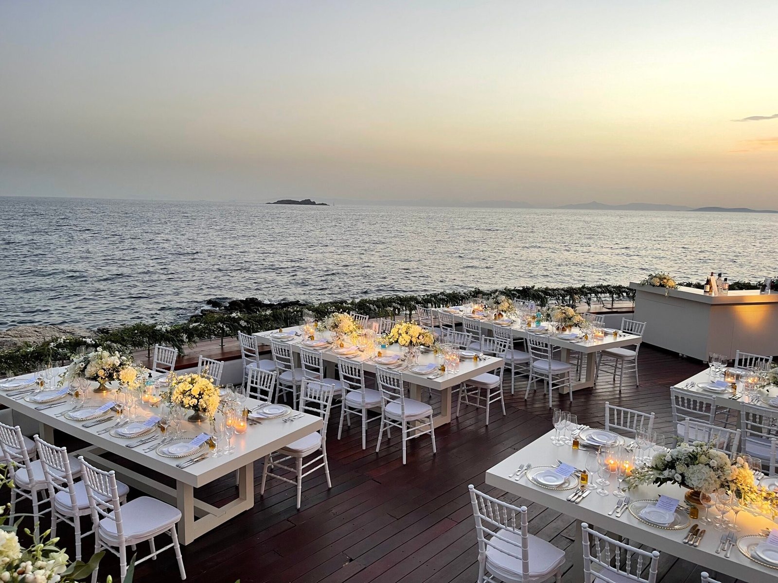 Long tables set for dinner beside the sea at sunset, Mathioudakis Exclusive Events