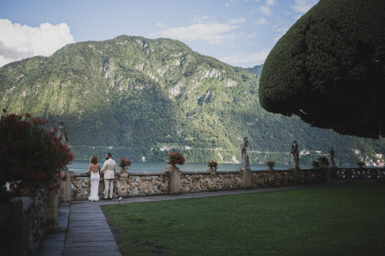 A couple at the far end of the lawn at Villa del Balbianello, the mountains rising across Lake Como, Matteo Cuzzola Photography
