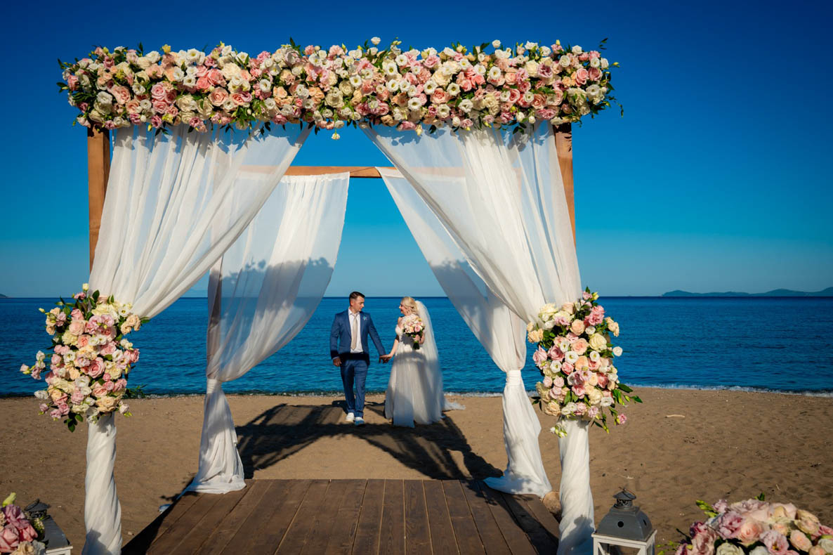 Couple walking to the floral arch on the beach, Mazal Weddings