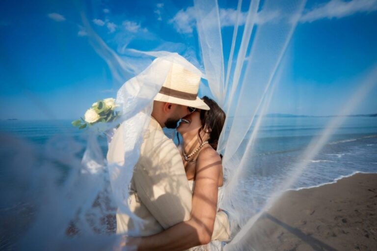 A couple embracing on the beach beneath a drifting veil, Mazal Weddings