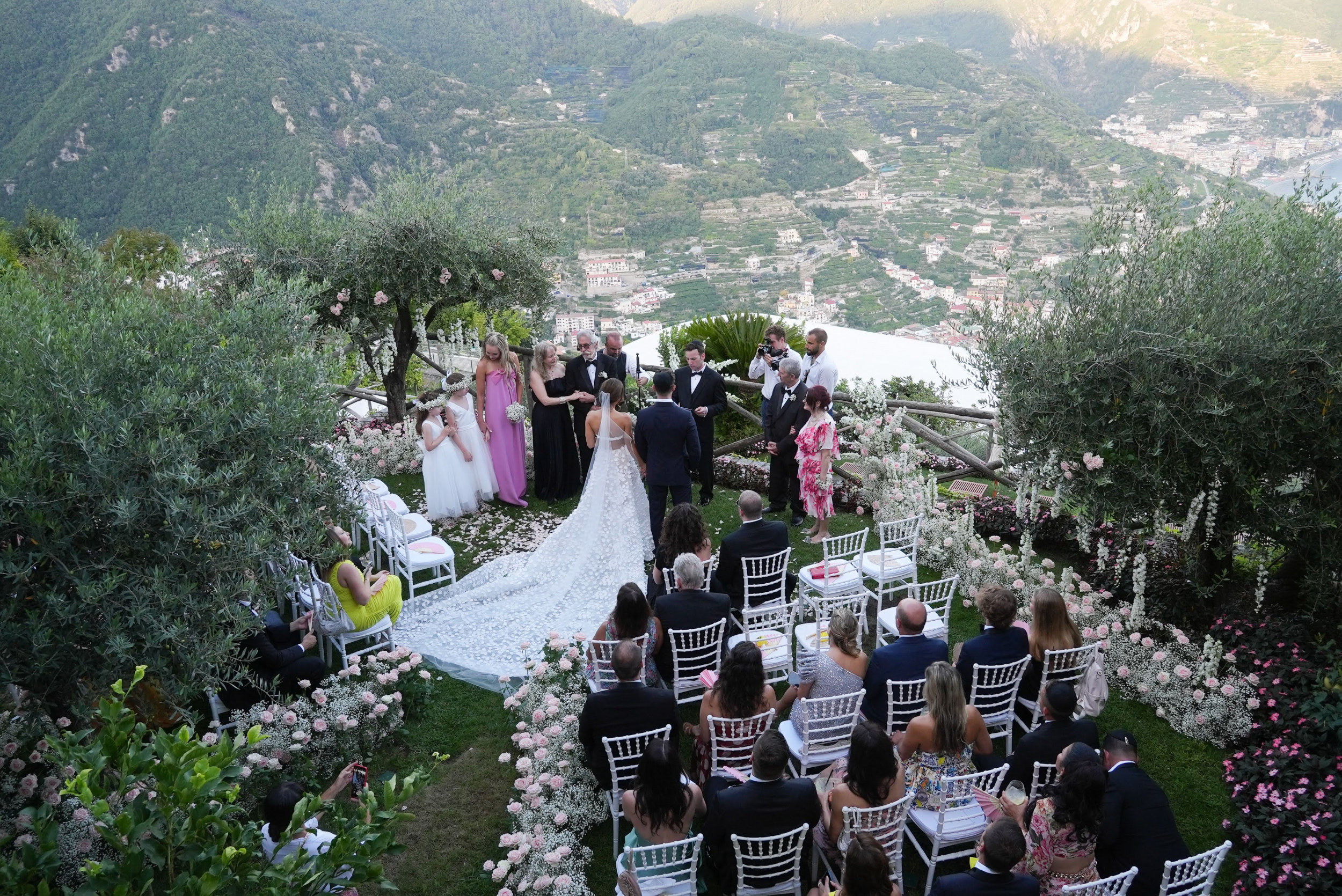 Garden ceremony among olive trees and white flowers, the terraced Amalfi Coast hillside falling away behind the guests, Med inStyle
