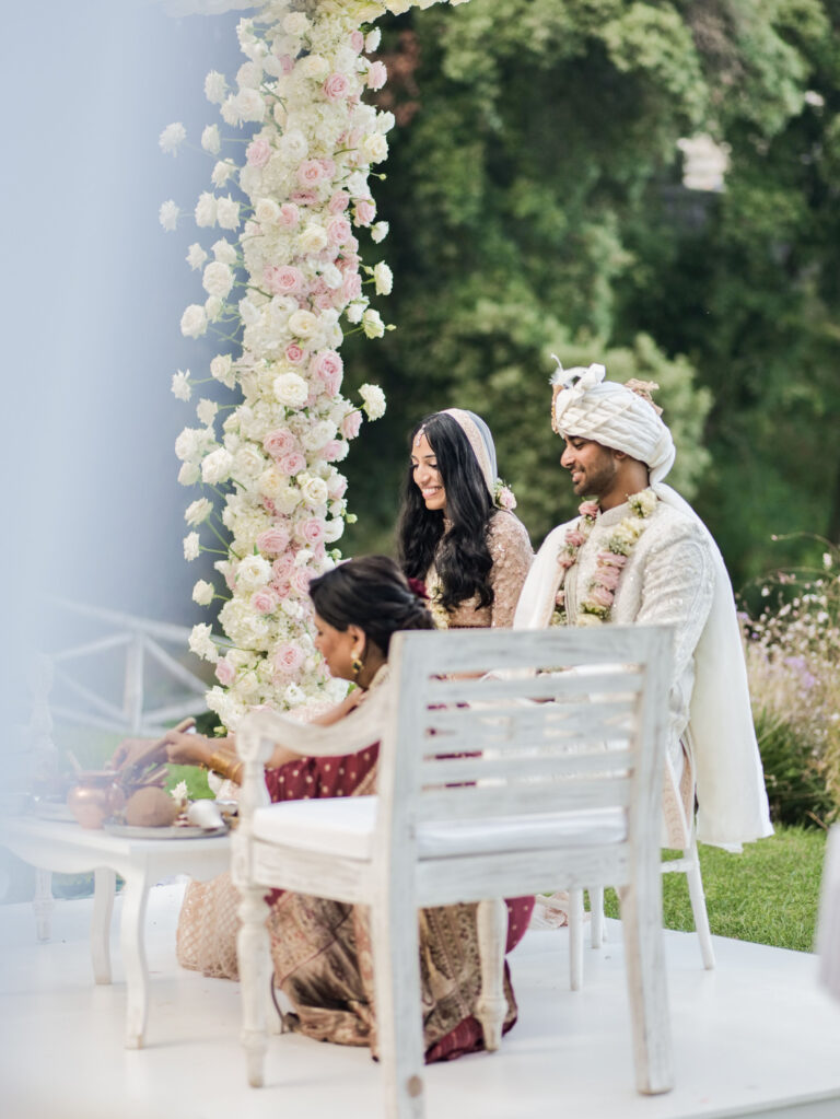An Indian wedding ceremony on a garden platform, a column of white and blush roses beside the couple, Med inStyle