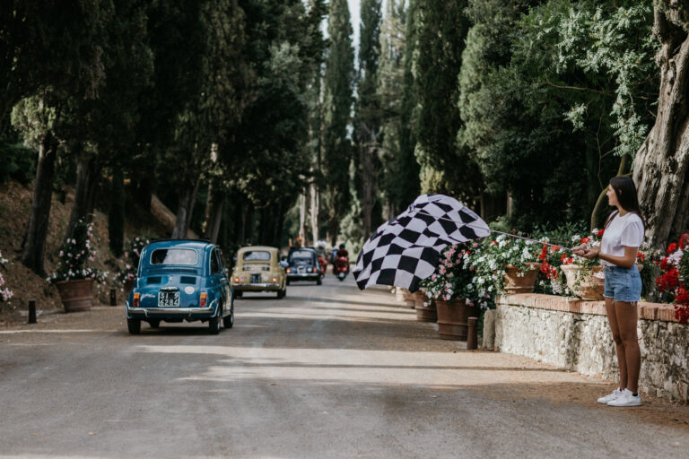 Vintage Fiat 500s driving down a cypress avenue as a guest waves a chequered flag, Med inStyle
