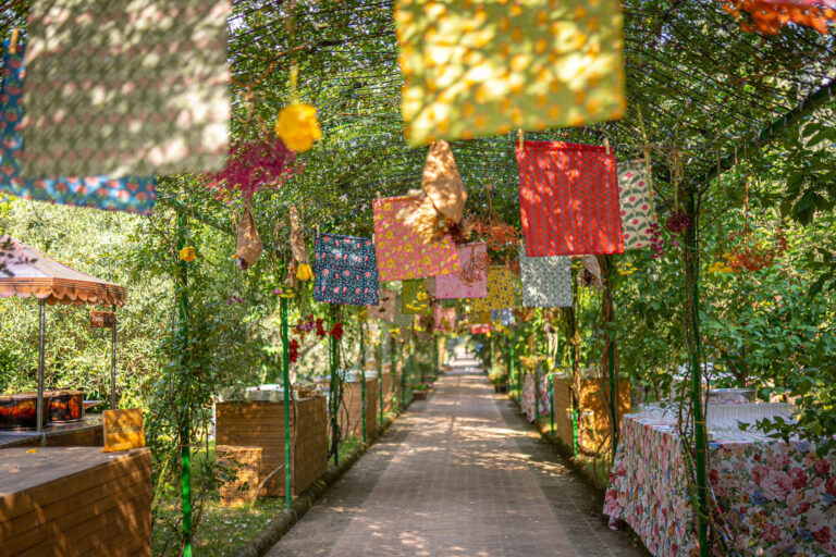 A garden pergola walk hung with squares of printed fabric and flowers, food stations and patterned tablecloths along the path, Med inStyle
