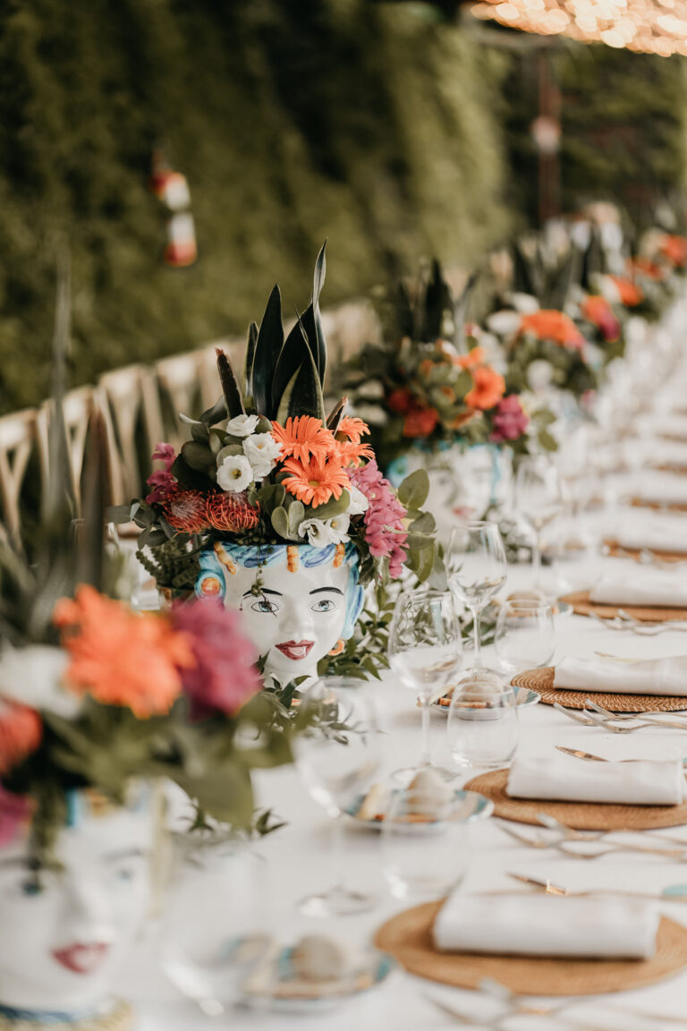 Ceramic head vases filled with orange and pink flowers along a long white-set table, Med inStyle