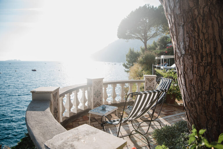 Striped deckchairs on a balustraded terrace above the sea, pines and the coast in the hazy light behind, Med inStyle