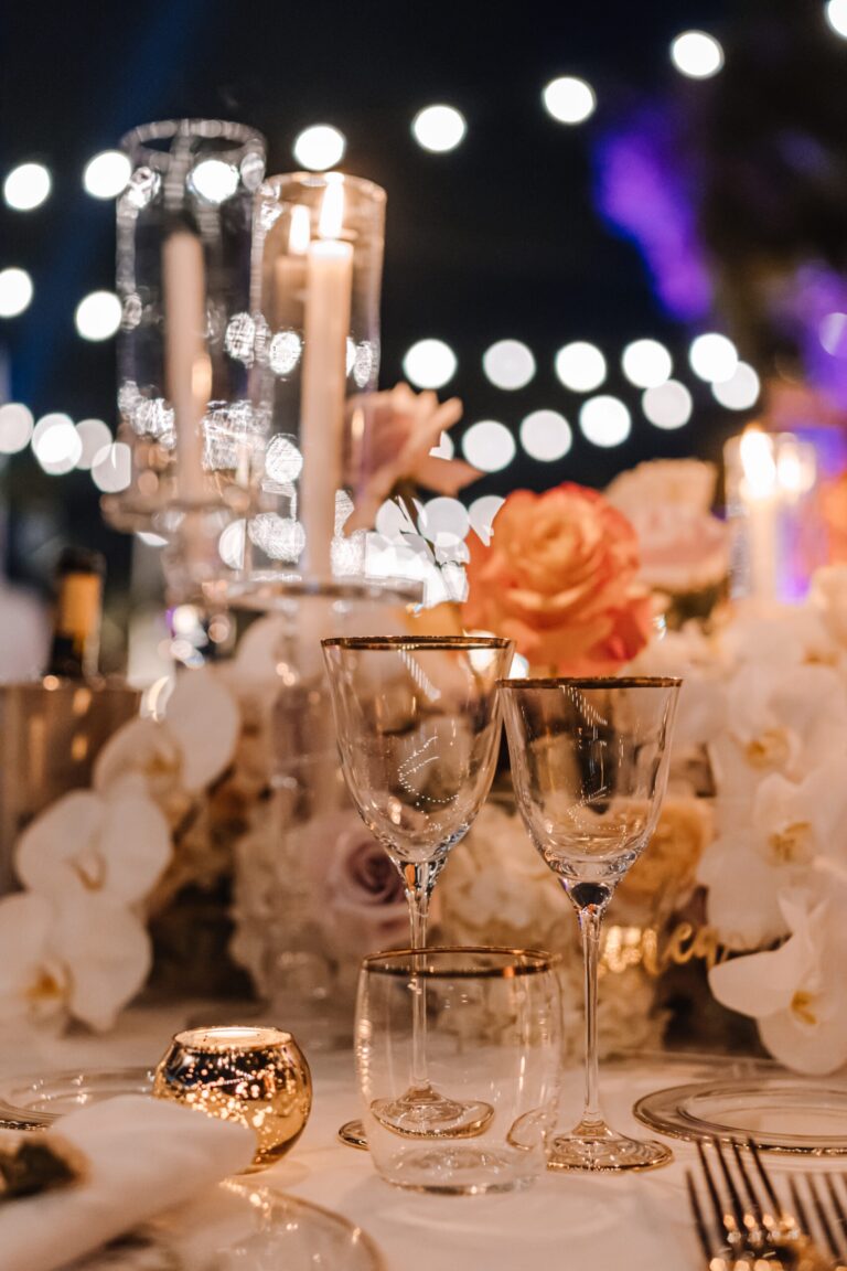 A glass candelabra of orchids, festoon lights behind, Meissa Eventi