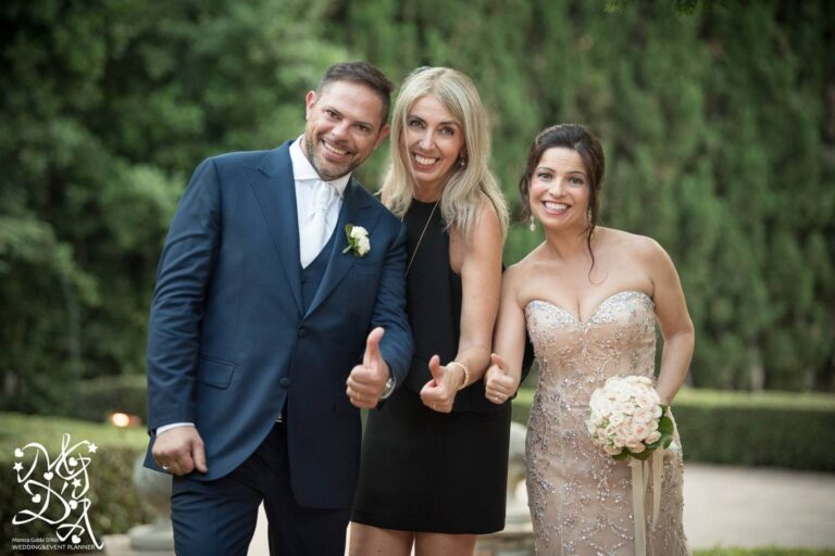 A bride in a white flower crown embraces Monica at a restaurant table behind glazed wooden doors, MGDA Events