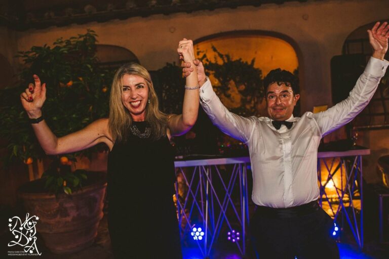 A bride in an embellished gown embraces Monica in a cypress garden, the groom beside them, MGDA Events