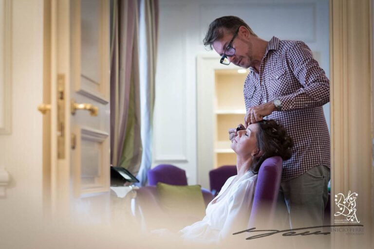 A hairstylist finishes a bride's updo in a suite with gilded door handles and lilac curtains, MGDA Events