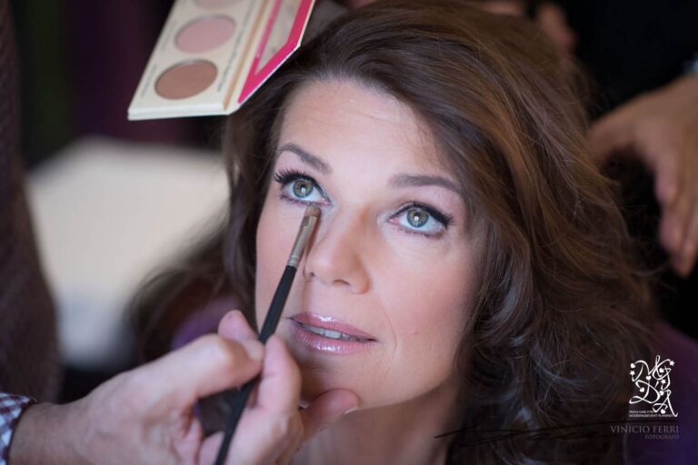 A make-up artist applies eyeshadow to a bride's eye, a contour palette held above, MGDA Events
