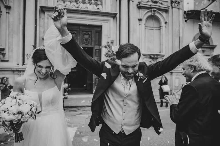 The groom throws his arms up as the couple leave the Church of Ognissanti through falling petals, Michele Monasta Photography