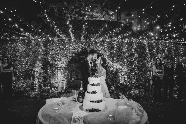 Cutting the cake under strings of lights in the garden at Villa di Striano, Michele Monasta Photography
