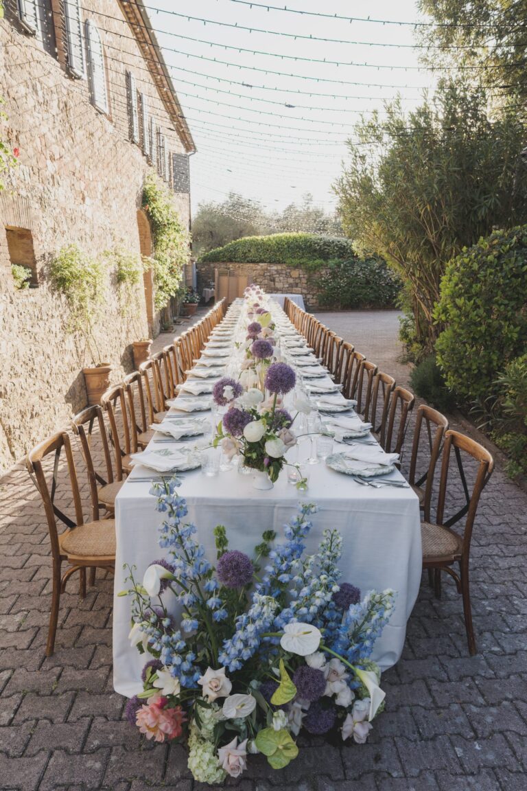 A single long table dressed with delphiniums and roses along the stone walls of Borgo Argiano, Michele Monasta Photography