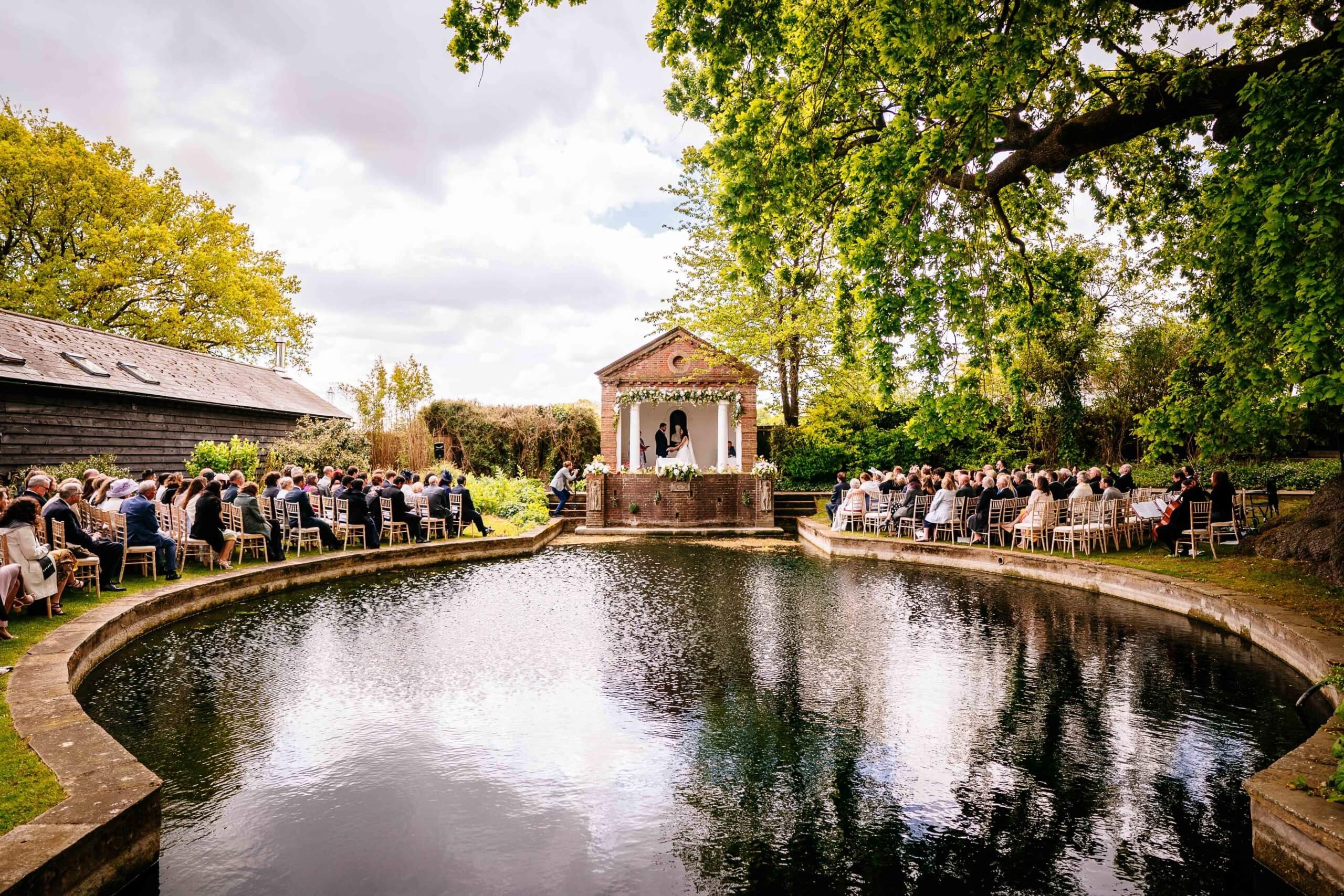 A civil ceremony at The Temple, guests seated around both banks of the pond under the great oak, Micklefield Hall