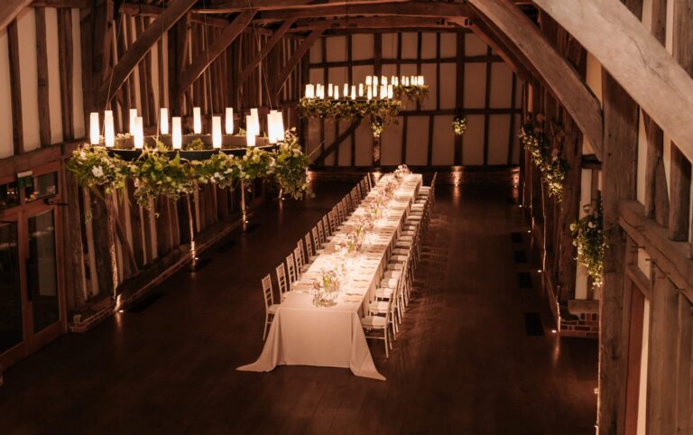 The Great Barn interior, long banquet tables by candlelight beneath a foliage chandelier, Micklefield Hall