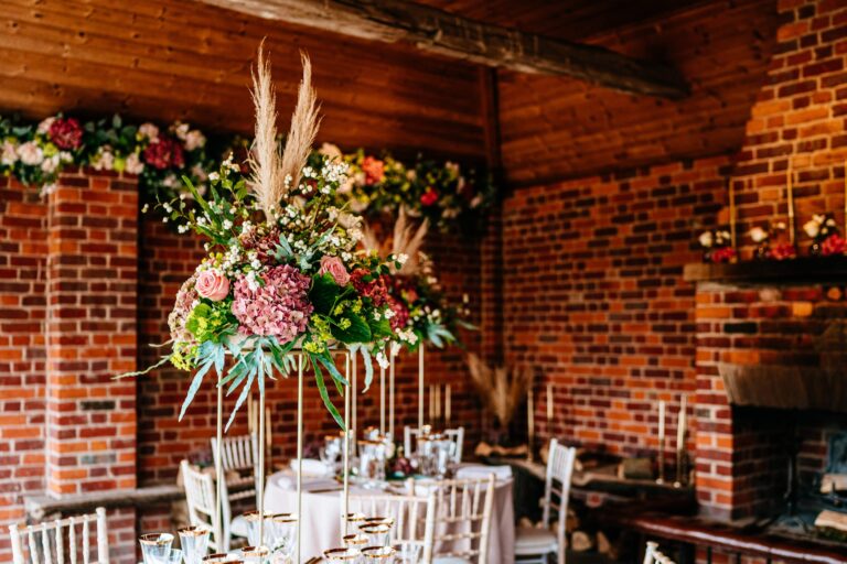 The covered loggia with a brick fireplace, tall florals and round tables, Micklefield Hall