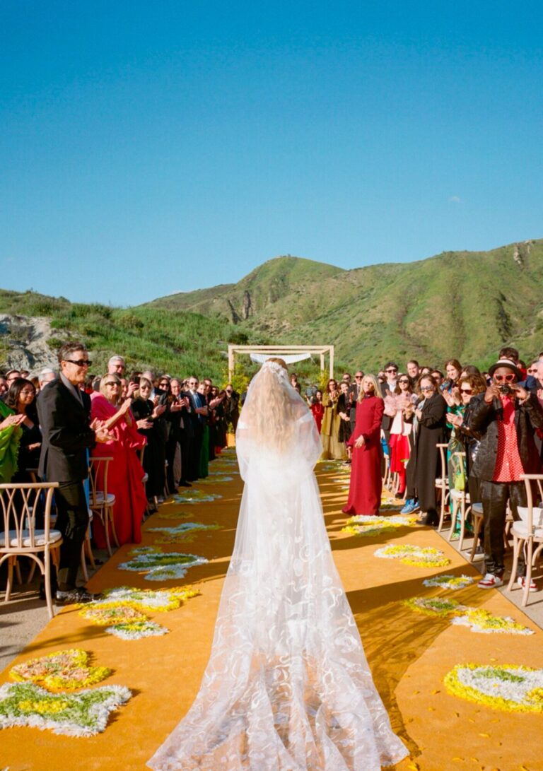 A bride walking a golden-yellow aisle towards guests in the hills, Mindy Weiss Party Consultants