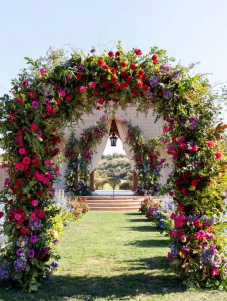 A large arch of red, pink and purple flowers framing a lawn, Mindy Weiss Party Consultants