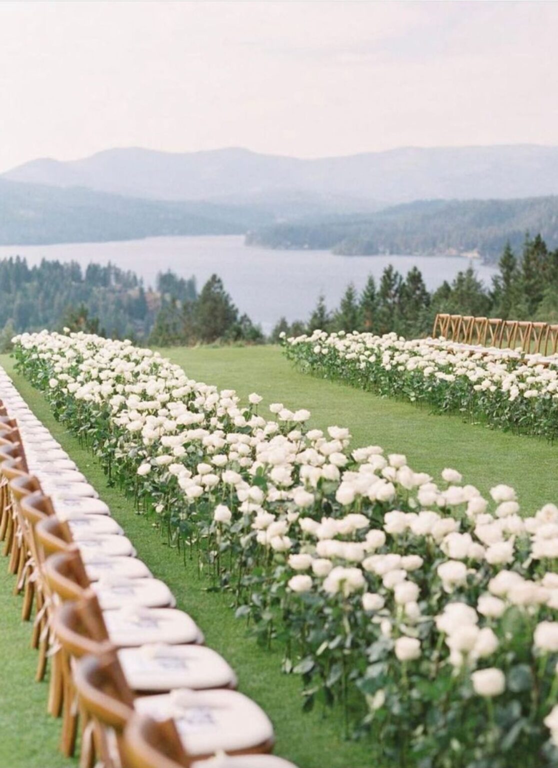 A lawn aisle edged with white flowers above a lake and mountains