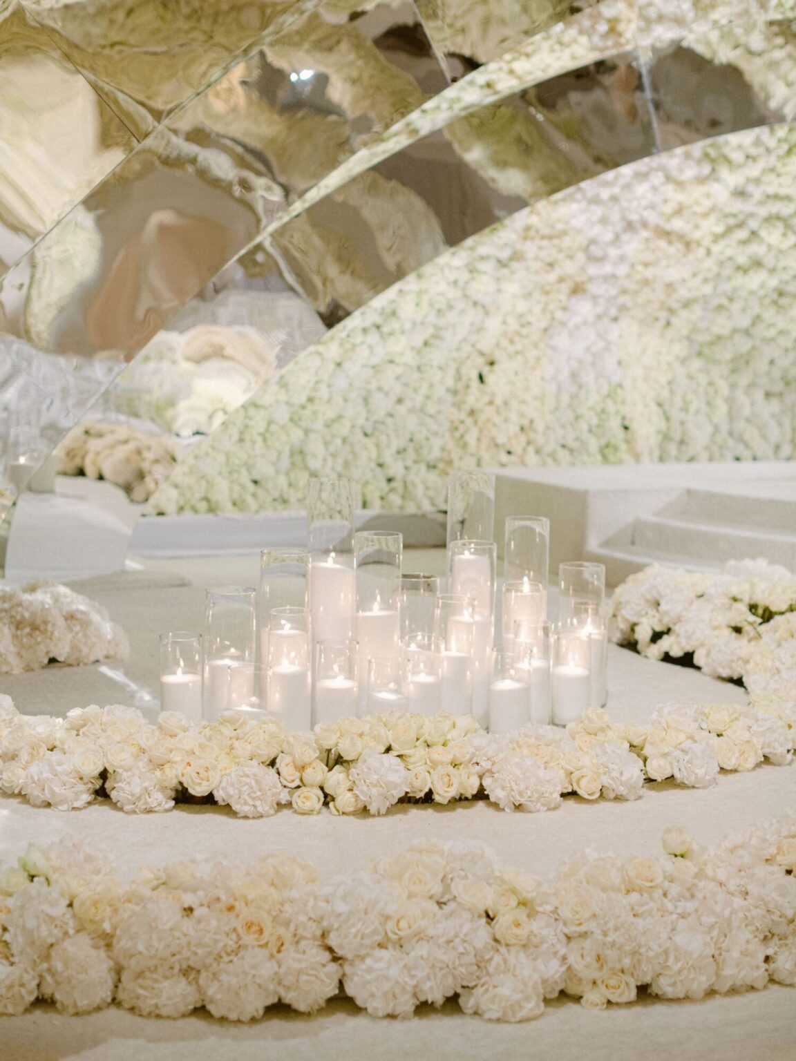 A mirrored vault banked with white flowers above a long table and candles