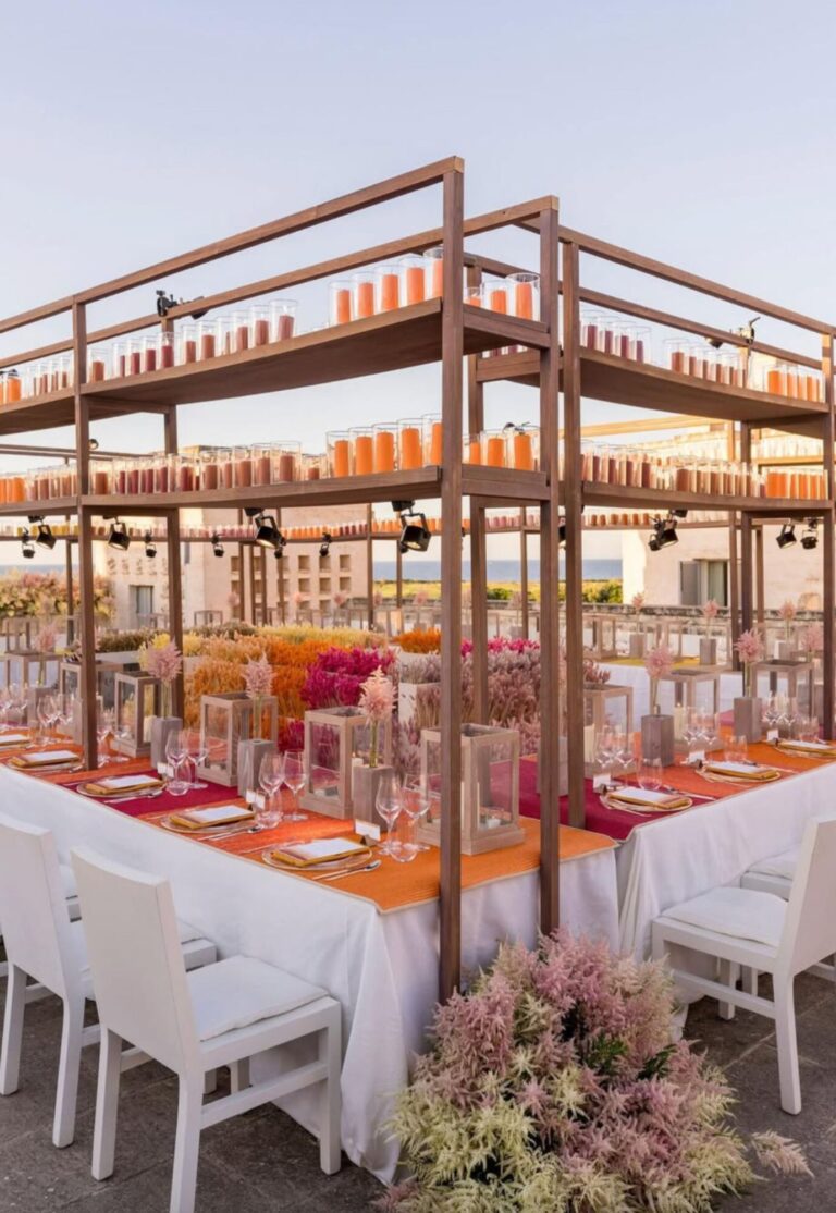 Tables on a terrace set in orange, pink and yellow with flower-filled shelving, Mindy Weiss Party Consultants
