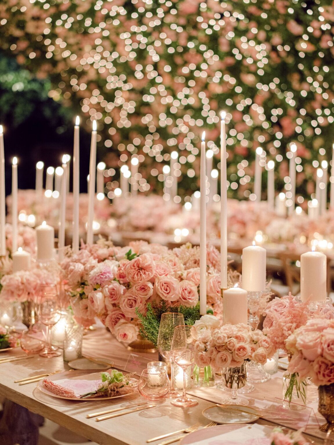 Long tables of tall candles and pink roses beneath a ceiling of blooms