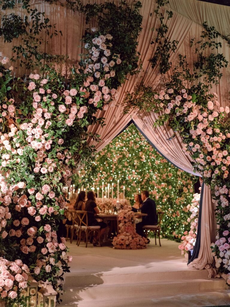 An arch of roses and draped fabric leading to a candlelit dining space, Mindy Weiss Party Consultants