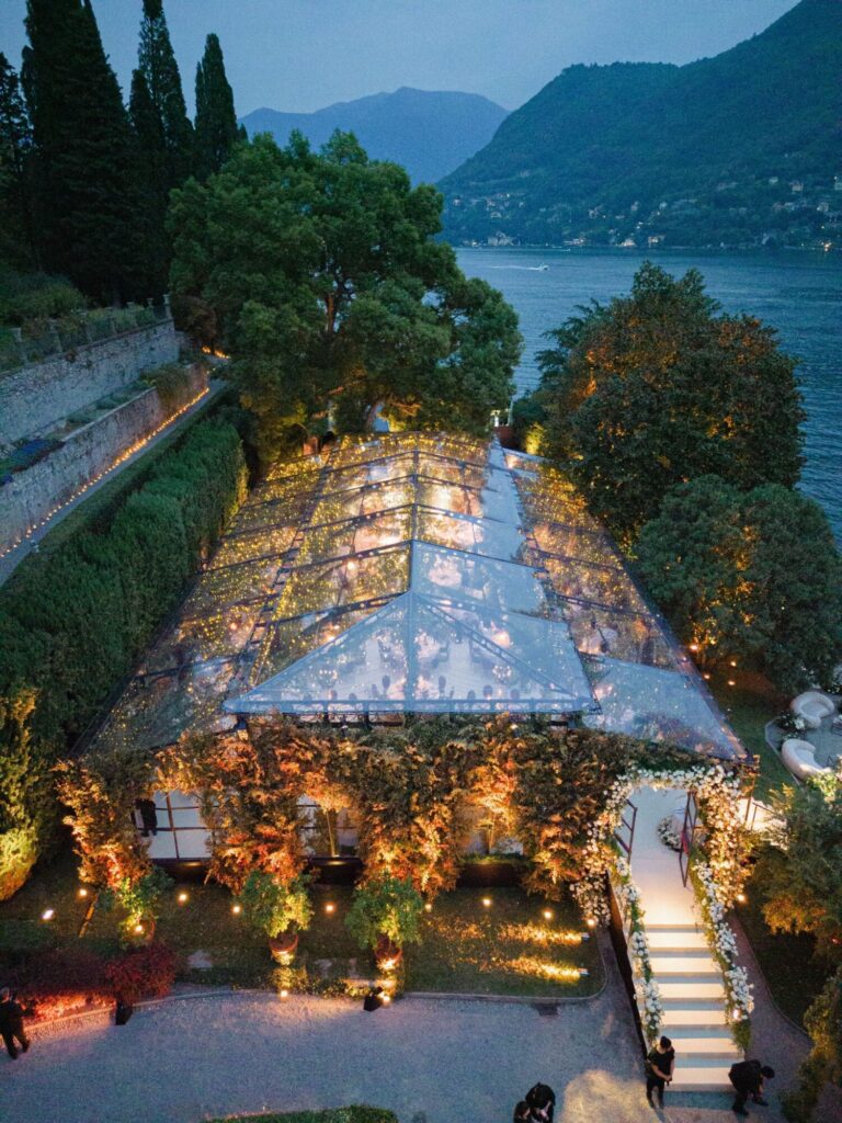 A glass-roofed marquee lit at dusk on a lakeside terrace, Mindy Weiss Party Consultants
