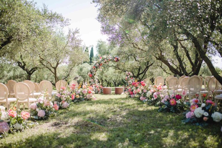 An aisle through an olive grove, the ground lined with coral and pink flowers, Mirko Zago, Sparkling Weddings and Events