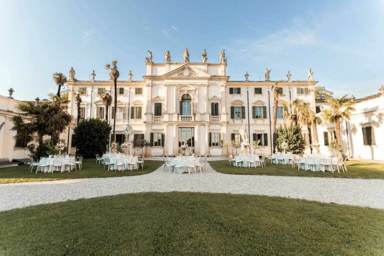A baroque villa with statues along its roofline, tables set on the lawn before it, Mirko Zago, Sparkling Weddings and Events