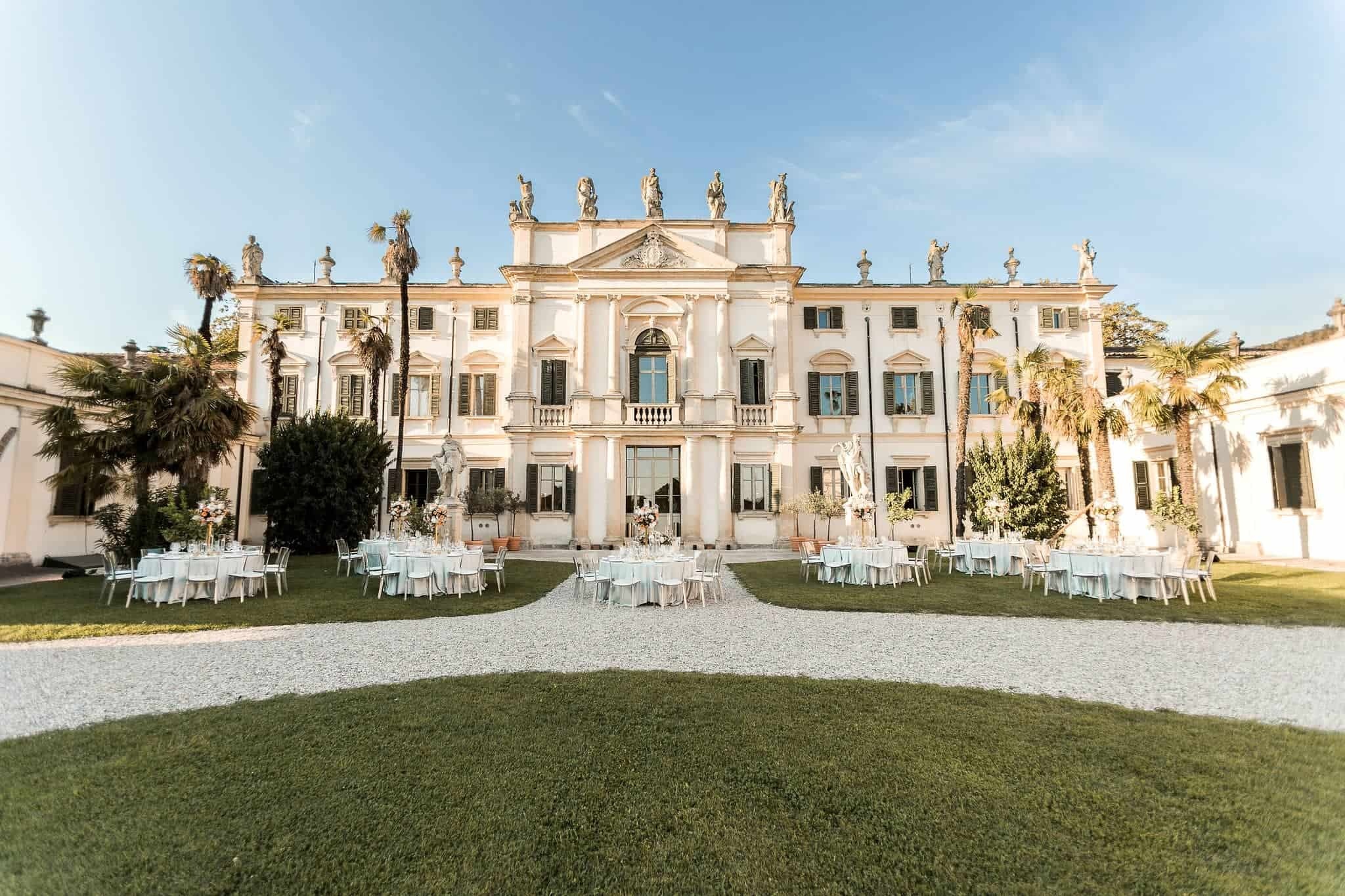 A baroque villa with statues along its roofline, tables set on the lawn before it, Mirko Zago, Sparkling Weddings and Events