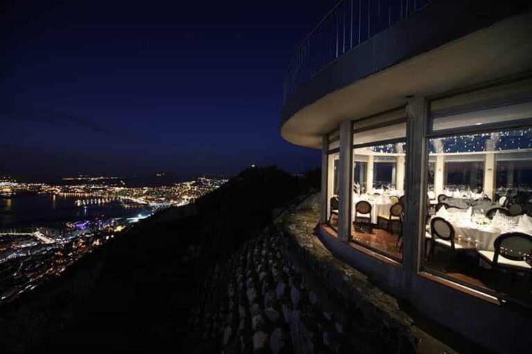 The suite at dusk, its curved glass facade lit, the town lights below, Mons Calpe Suite