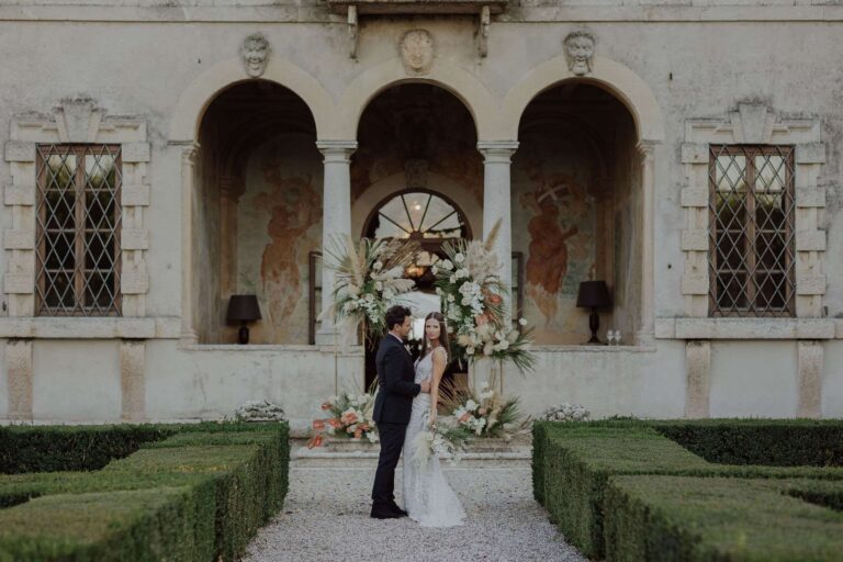 Couple before a frescoed loggia framed by pampas and dried flowers, an intimate wedding in Verona, More Than Weddings