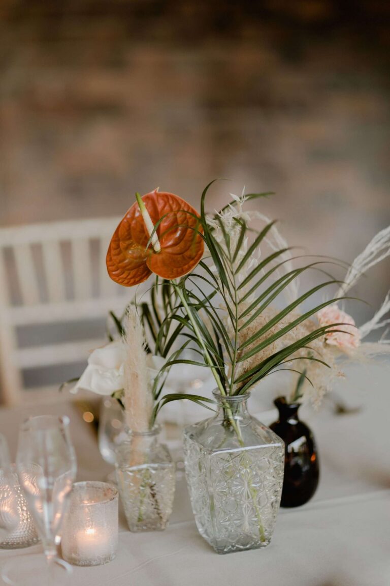 Centrepiece of orange anthurium and palm in glass vases, More Than Weddings