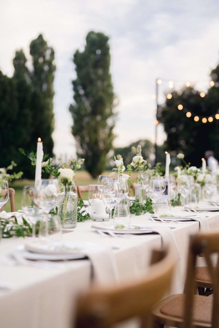 Outdoor table set with white flowers and tapers beneath tall poplars, More Than Weddings