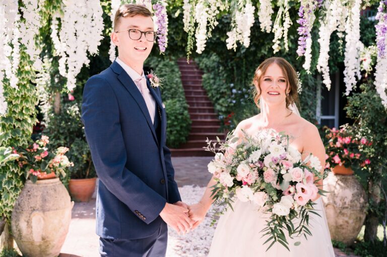 The couple hand in hand under hanging wisteria, terracotta urns either side, Amalfi Coast, Mr and Mrs Wedding In Italy