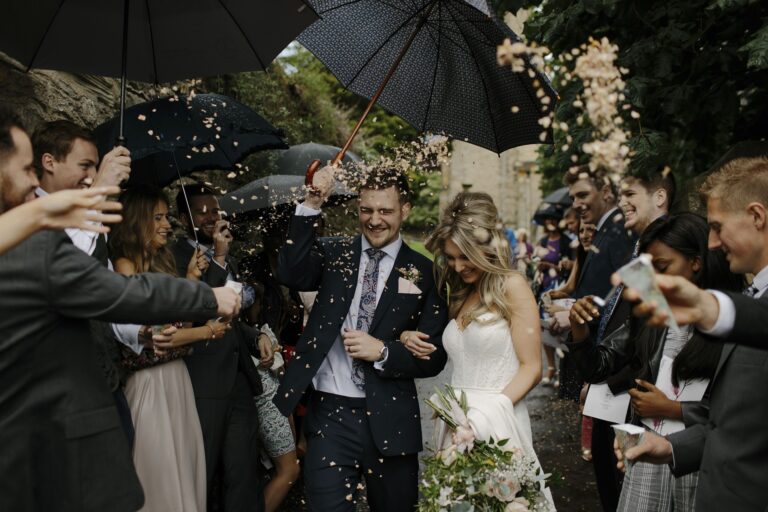 Guests throwing confetti under black umbrellas as the couple leave the ceremony, Mr and Mrs Wedding In Italy